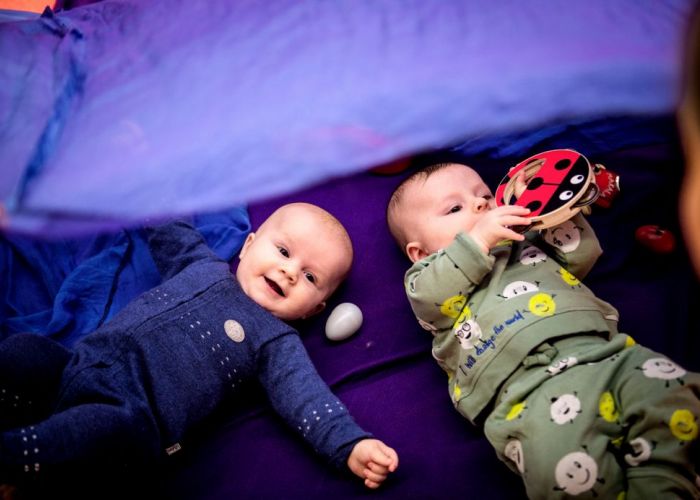 Bilde av to babyer som ligger på en lilla matte på gulvet.