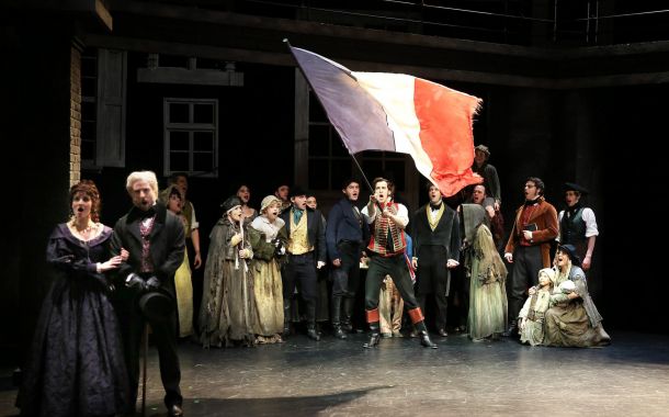 Skuespillere i kostymer på en scene. En mann holder et stort fransk flagg.