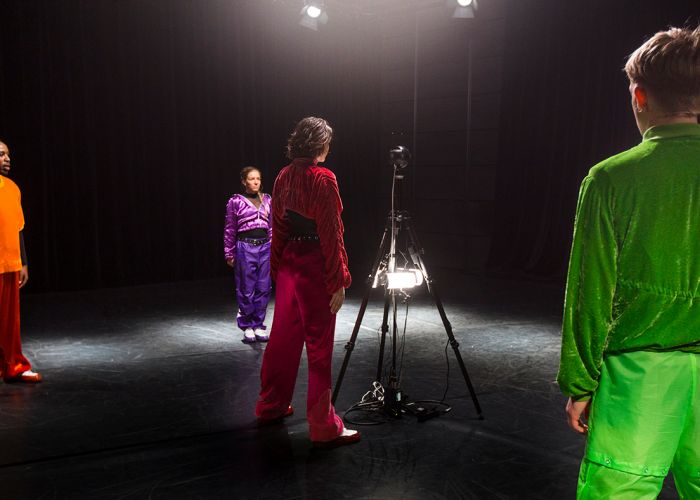 Bilde av fire unge voksne i fargerike treningsklær som står rundt et kamera.