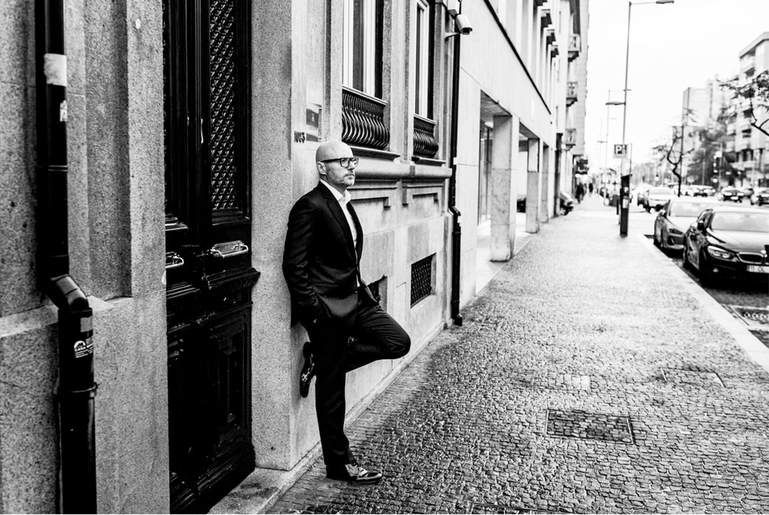 mann som poserer inntil en bygning i dress - bildet er i sort hvitt