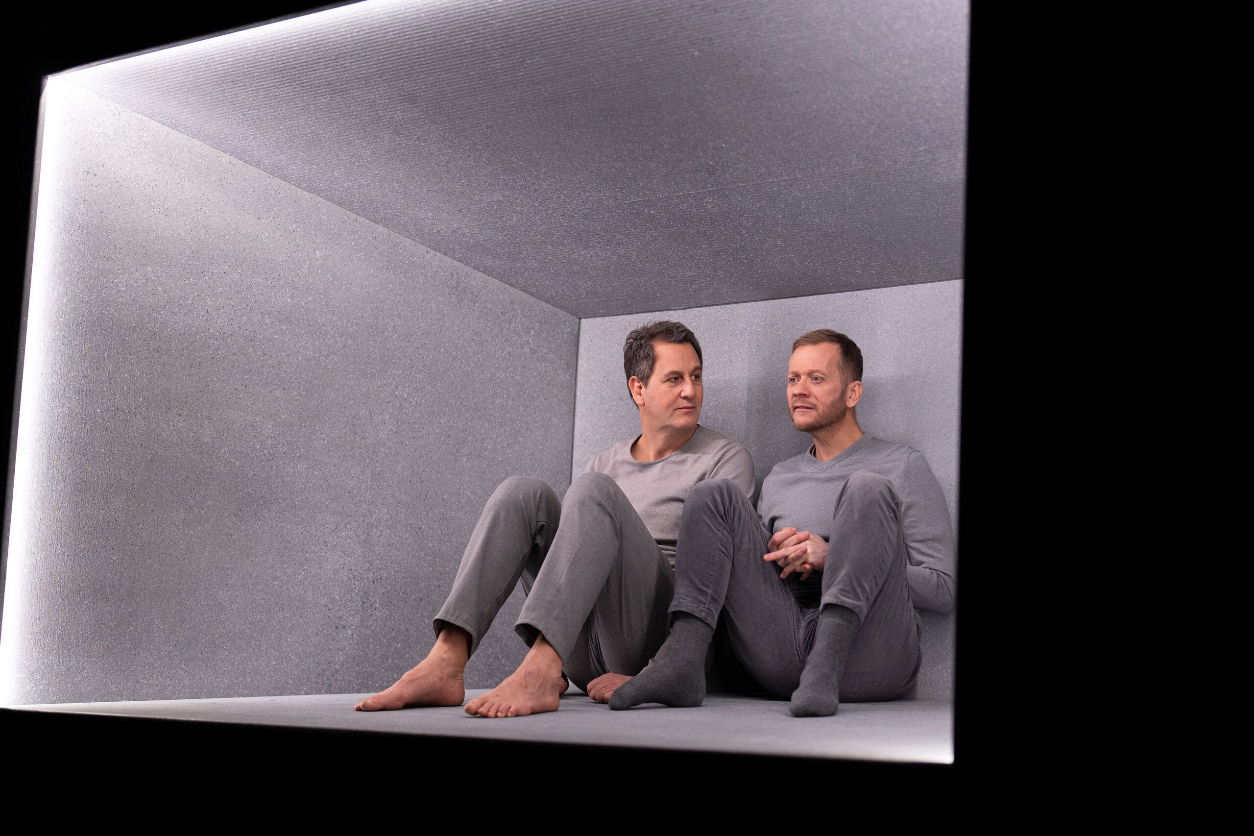 Skuespillere Henrik Rafaelsen og Morten Espeland som karakterene Den eine og Den andre i Eg er vinden. De er ikledd grå klær, og sitter i en grå, lysende, svevende boks.