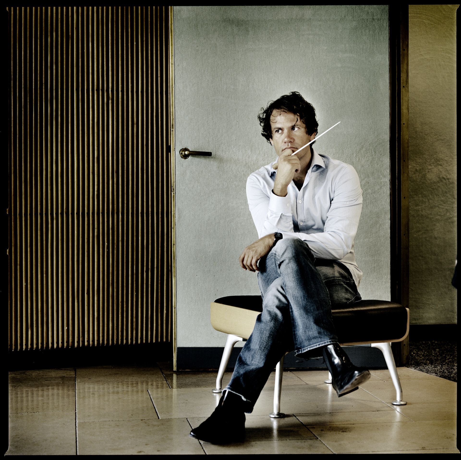 en mann i hvit skjorte og jeans som sitter på en puff i et trefarget rom