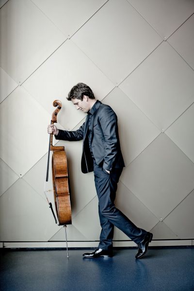 Cellist Maximilian Hornung foran en vegg med cello i hånden