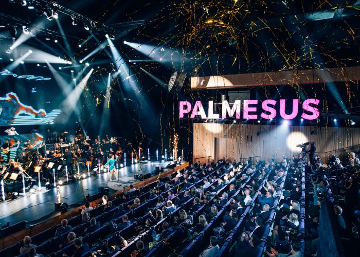 Bilde av publikum og scene med artister. Logo for Palmesus synlig i rosa i bildet.