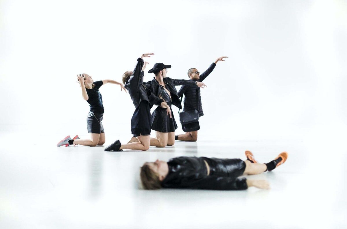 Bilde av fem mennesker som danser i sorte skinnklær i et helt hvitt rom.