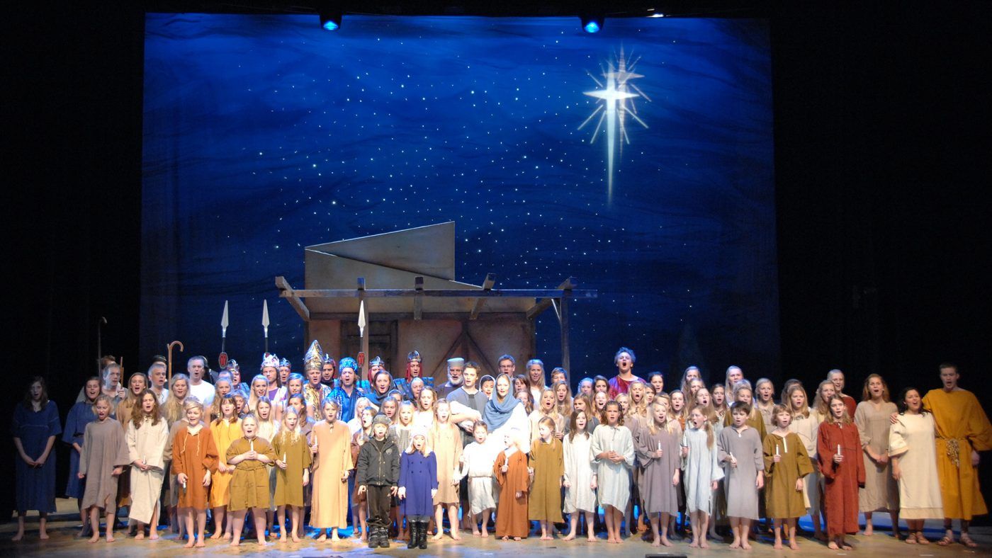 Bilde av mange barn i kostymer på en scene. I bakgrunnen skinner en stjerne.
