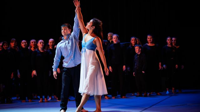 En ung mann og ung kvinne som danser sammen. I bakgrunnen skimtes et kor kledd i sort.