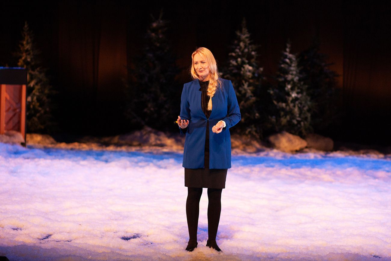 Kvinne med langt lyst hår i flette. Hun står på en scene dekket med snø.