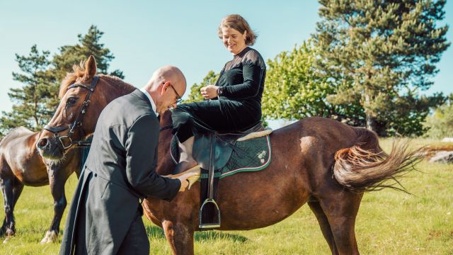 Lars Lunde setter en sko på foten til Hilde Garby Lunde som sitter på en hest