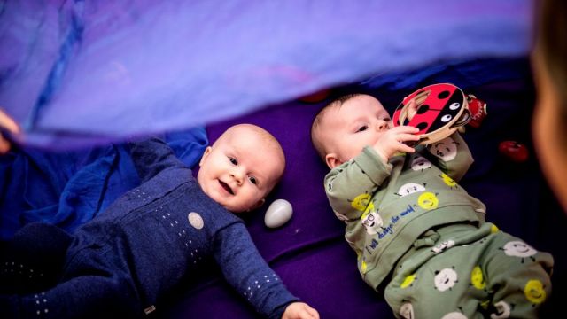 Bilde av to babyer som ligger på en lilla matte på gulvet.