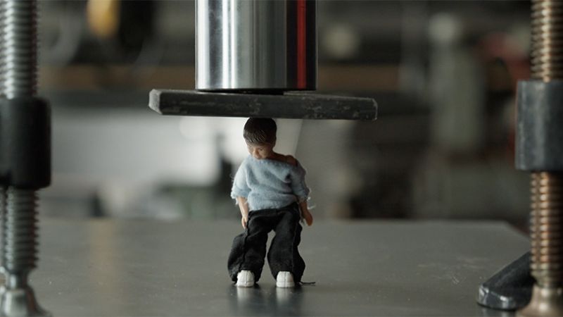 Bilde av guttedukke som blir skvist under et stempel.