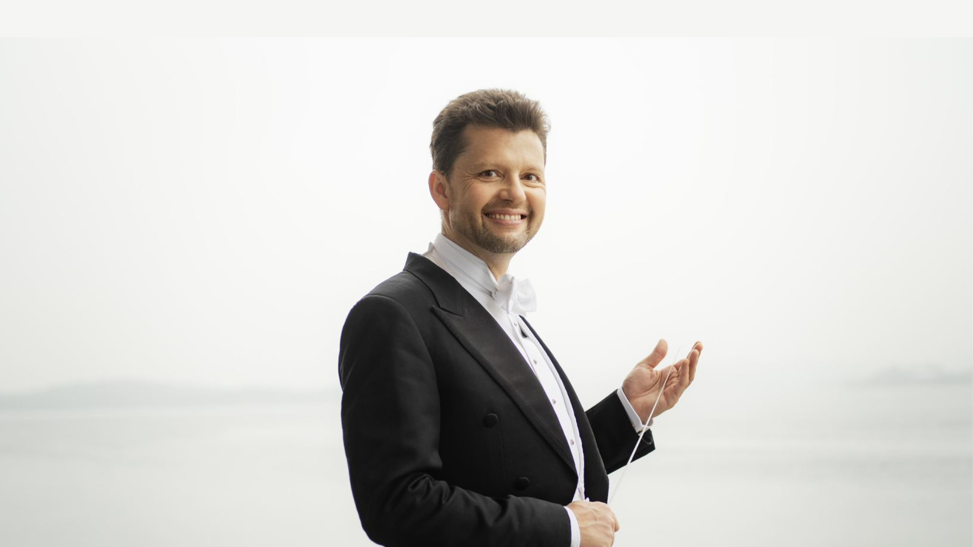 en mann I sort dress og hvit skjorte som poserer foran et tåkete hav