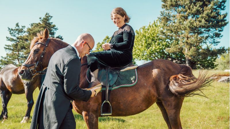 Lars Lunde setter en sko på foten til Hilde Garby Lunde som sitter på en hest