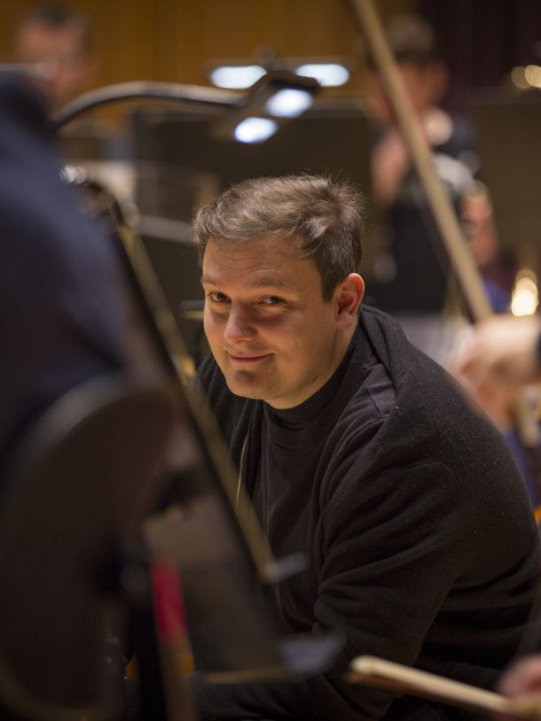 smilende musiker med brunt hår titter frem mellom andre musikere