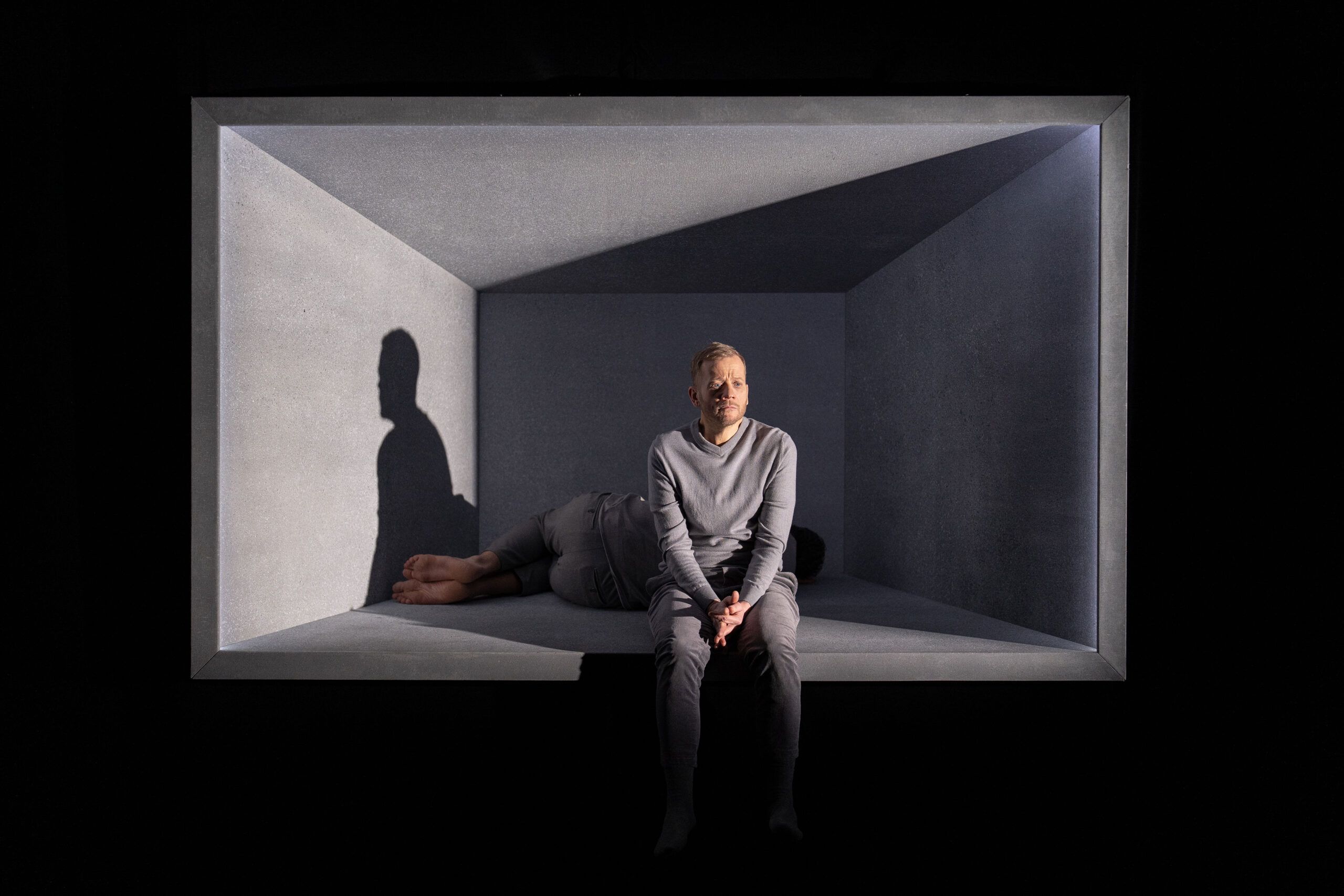 Skuespillere Henrik Rafaelsen og Morten Espeland som karakterene Den eine og Den andre i Eg er vinden. De er ikledd grå klær, og sitter i en grå, lysende, svevende boks.
