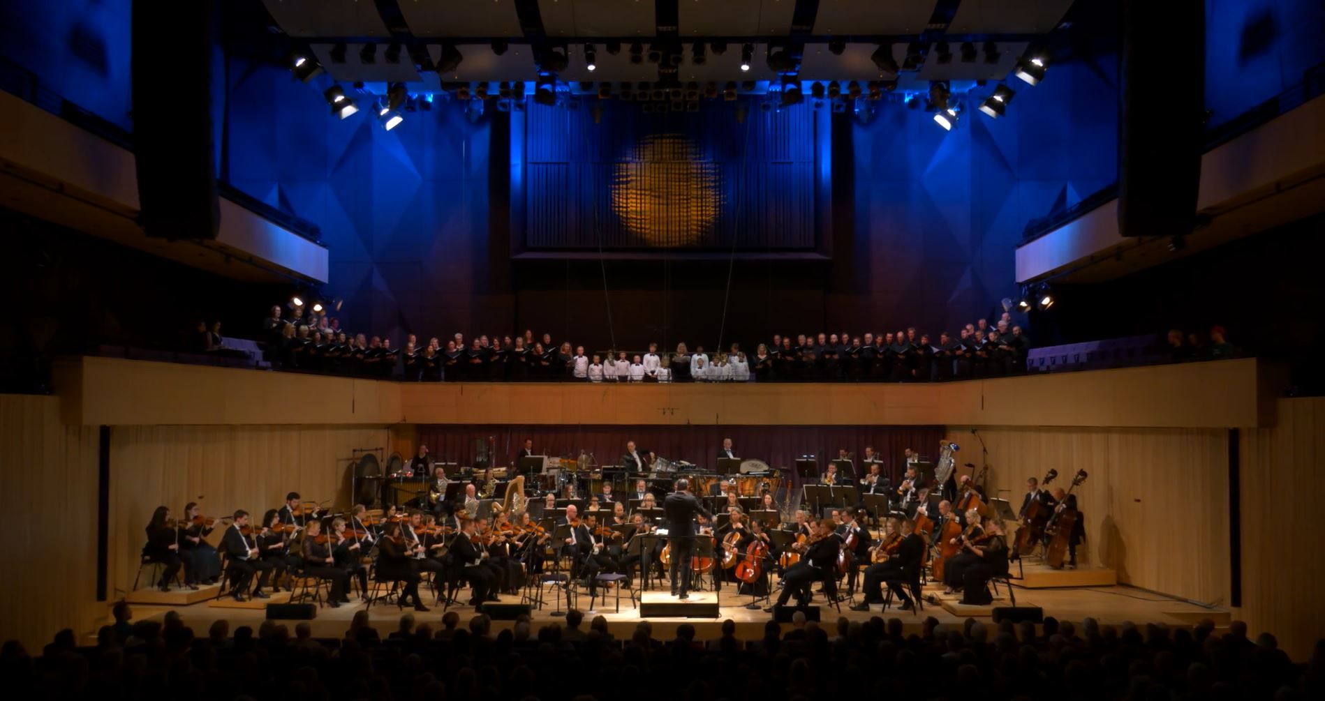 Bilde av et symfoniorkester og kor på en scene.