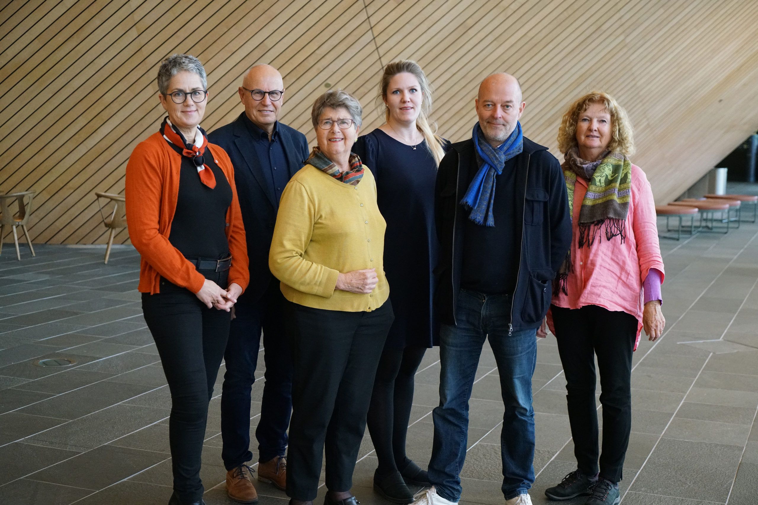 seks smilende mennesker oppstilt i en foaje