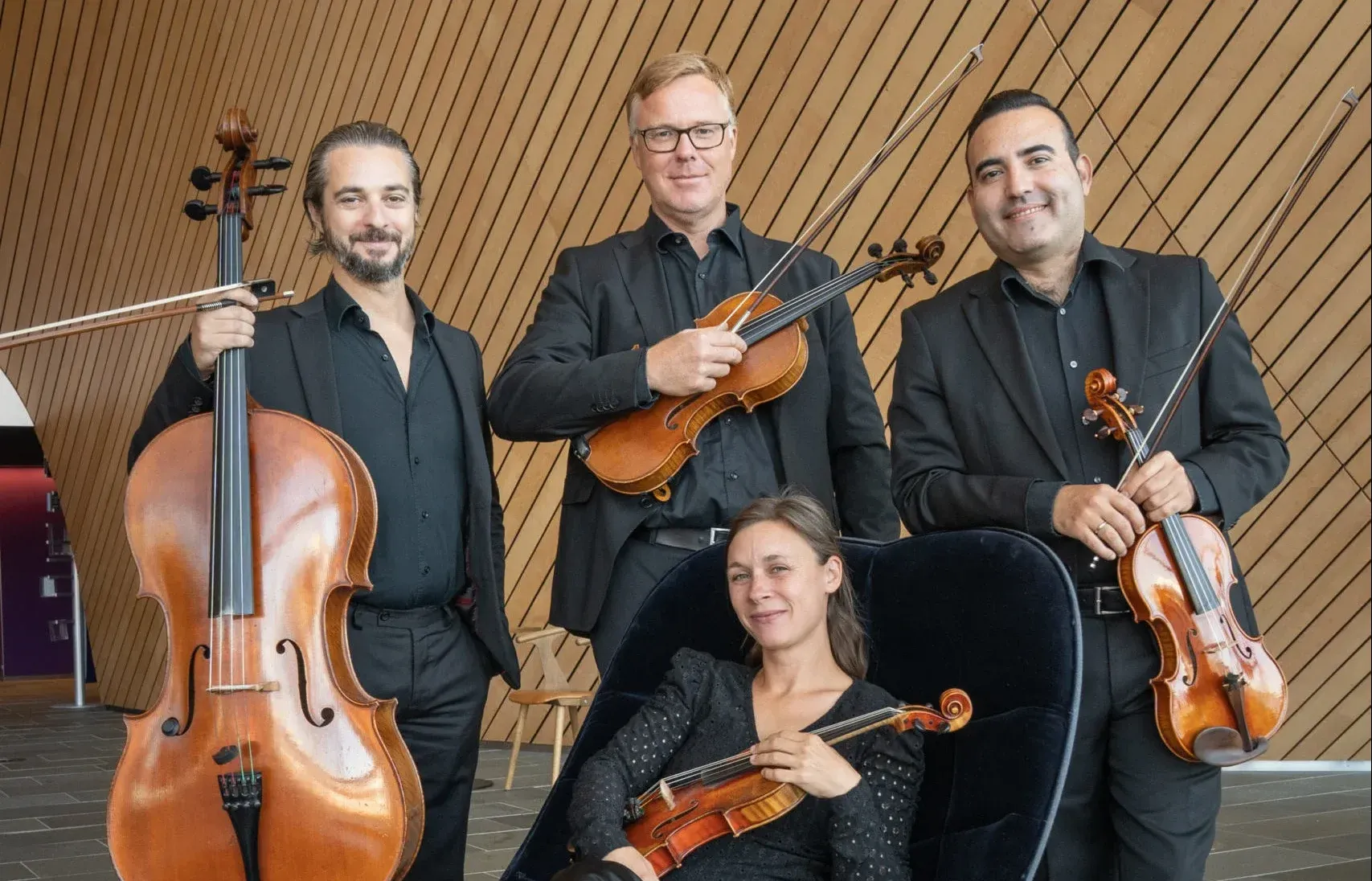 fire smilende mennesker som poserer i sorte antrekk med instrument