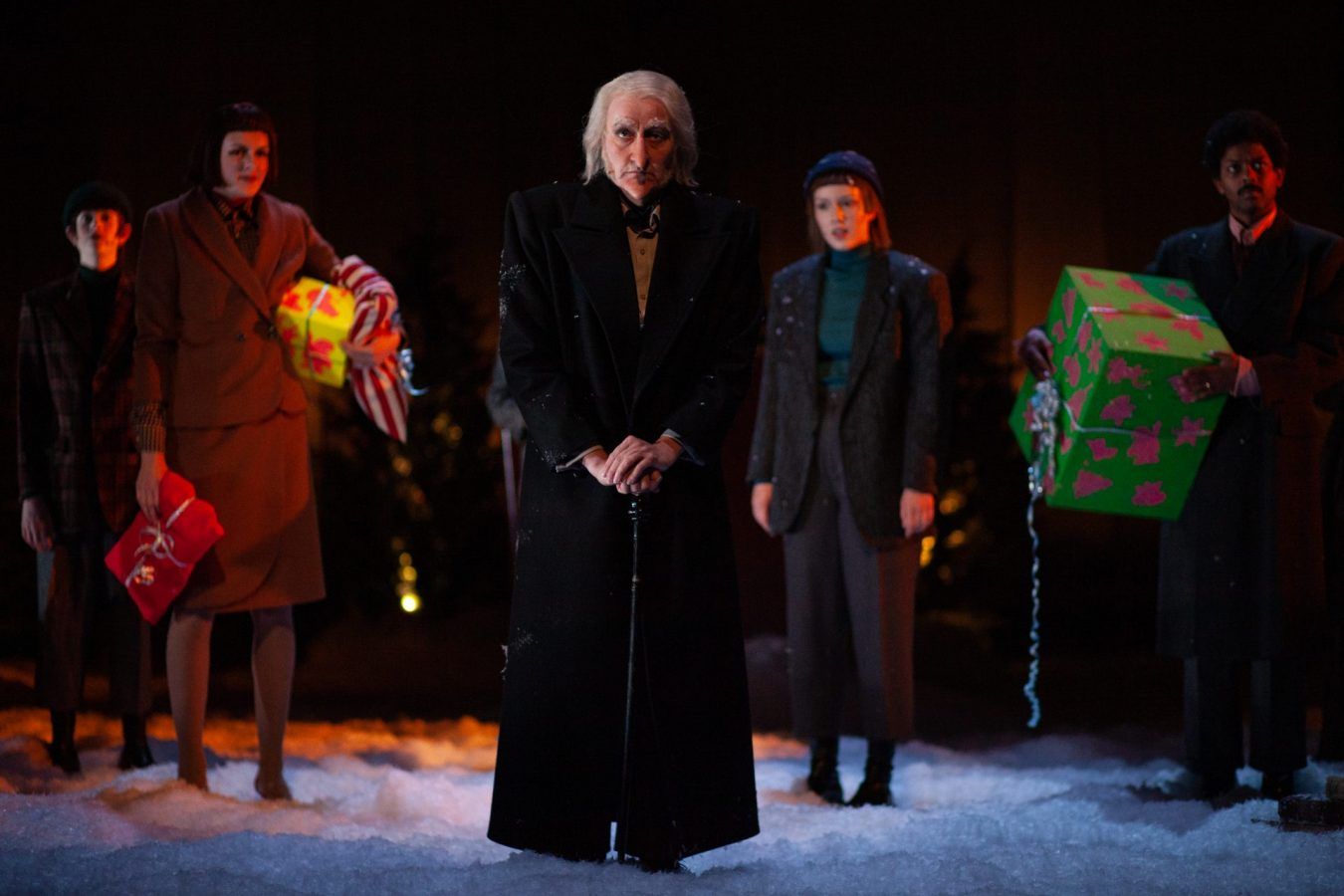 Fire skuespillere fra forestillingen En julefortelling som står samlet på en scene med kunstig snø rundt.