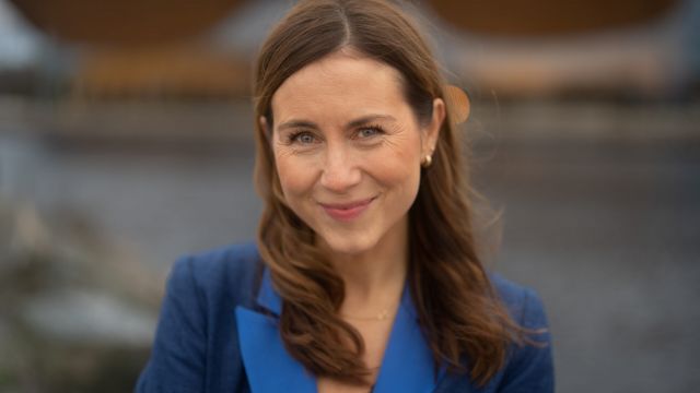 portrettkvinne smiler foran en vegg i blå jakke