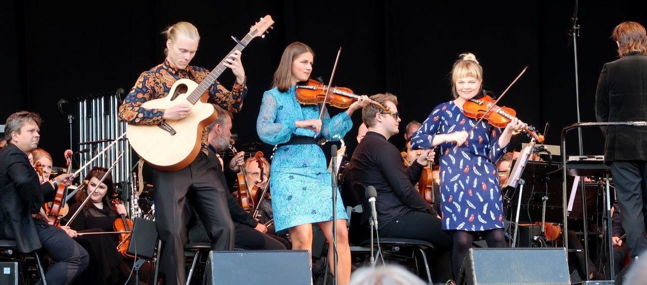 flere musikere i fargerikt tøy på en scene med fiolin og gitar. 