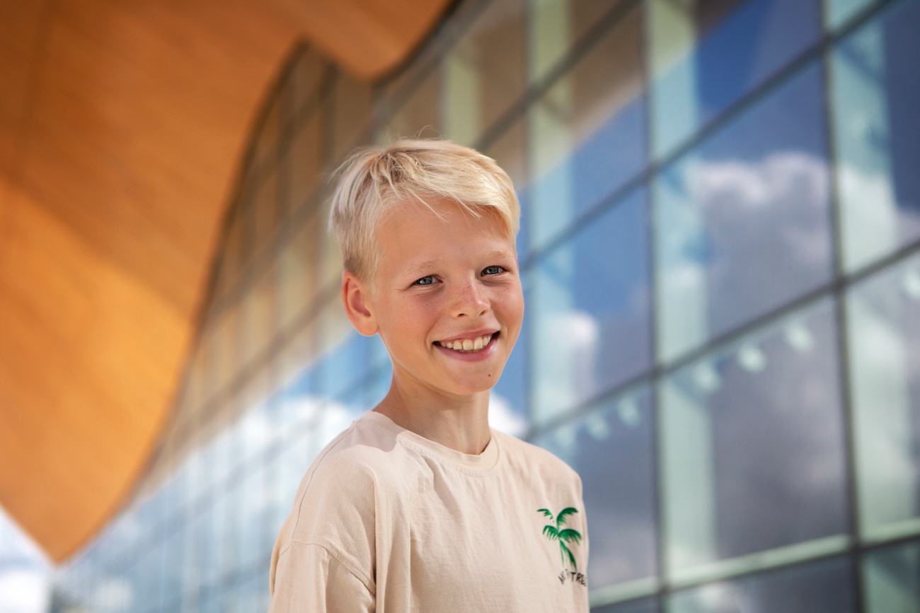 Bilde av gutt med lyst hår som smiler foran et bygg