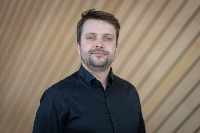 Portrettbilde av en smilende mann i mørk blå skjorte.