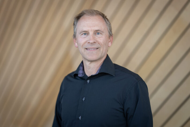 Portrettbilde av en mann i blå skjorte som ler.