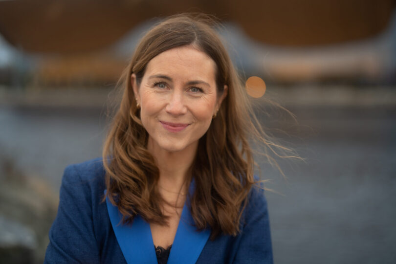 Portrettbilde av en smilende kvinne i blå dressjakke utendørs.