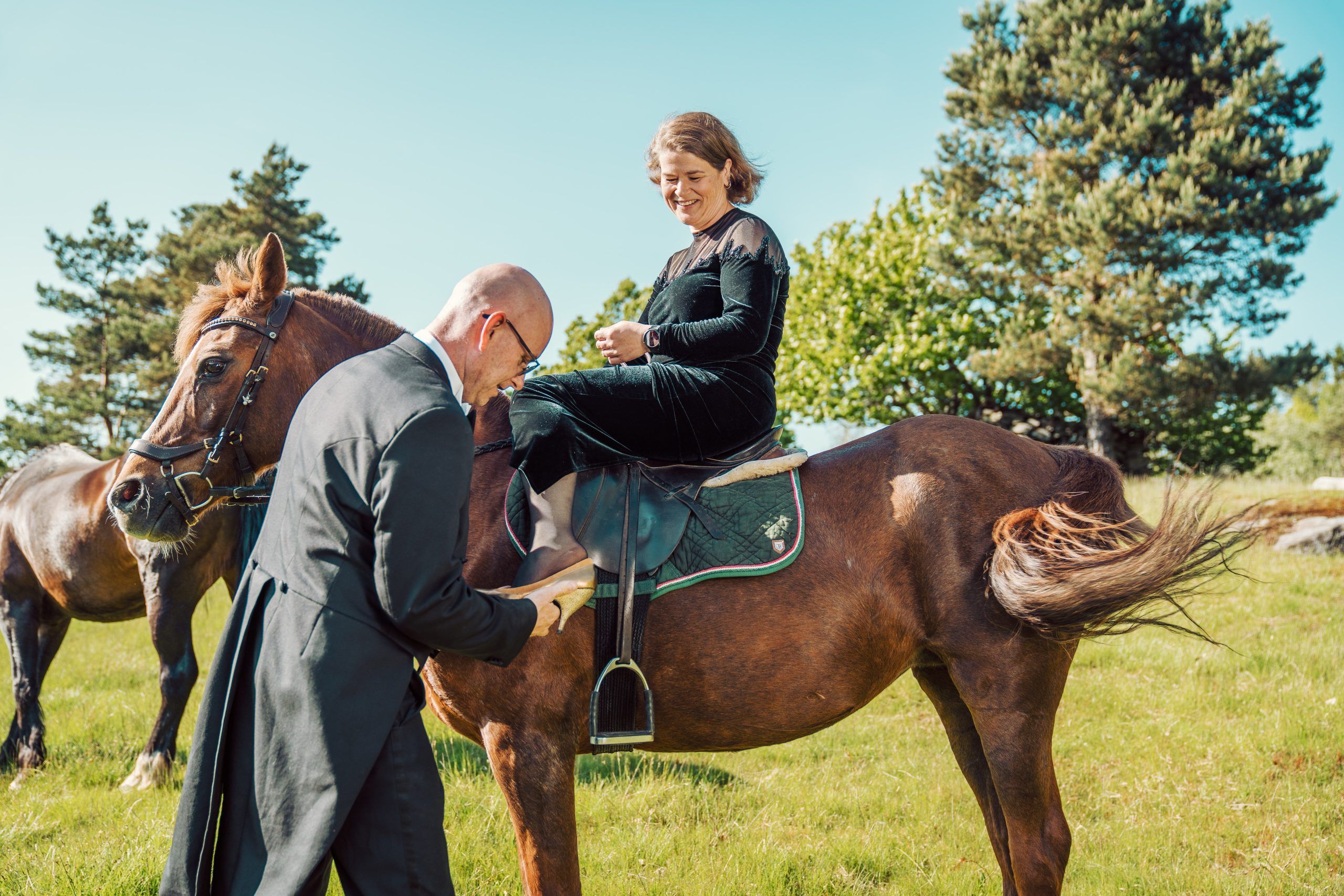 Lars Lunde setter en sko på foten til Hilde Garby Lunde som sitter på en hest
