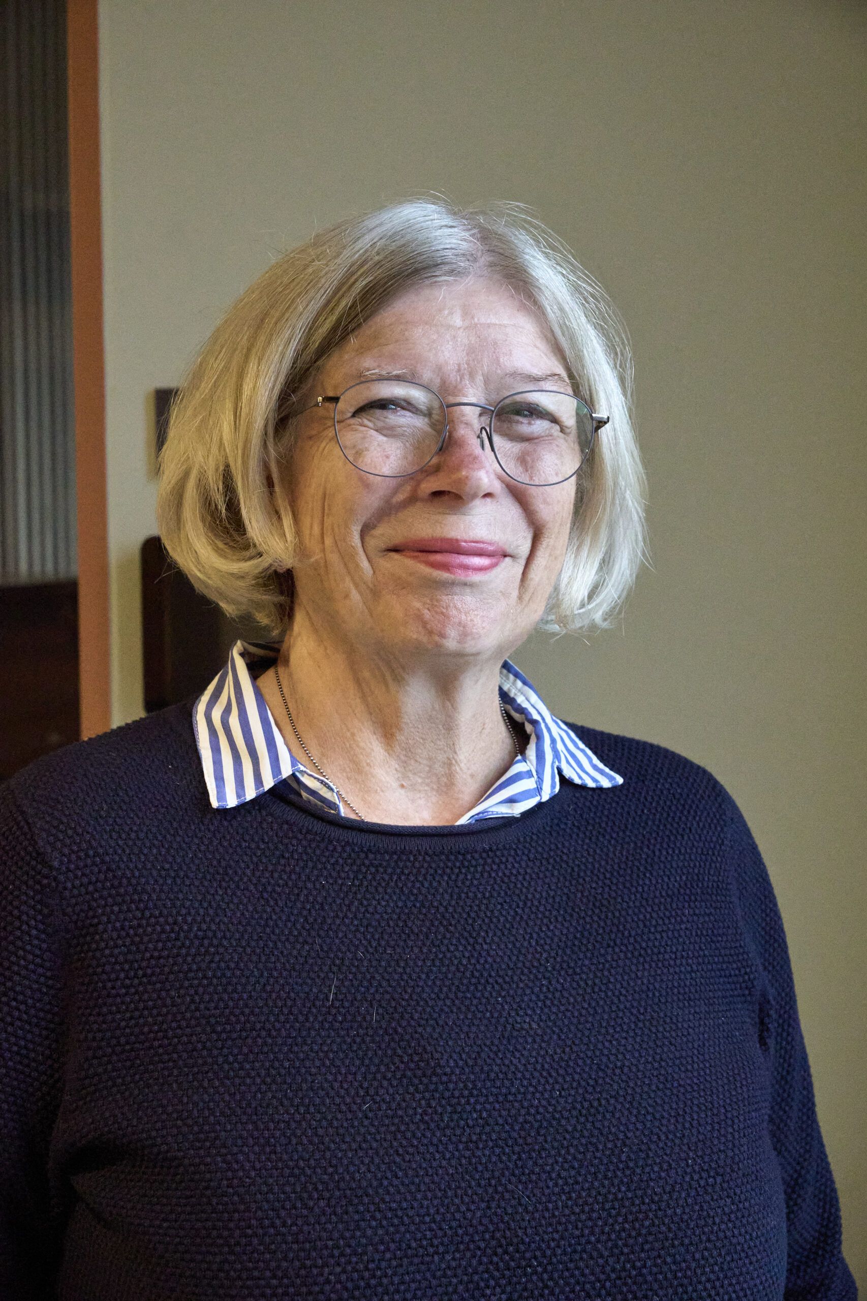 Randi Guri Jessen smiler inn i kamera, hennes mann synger i koret.