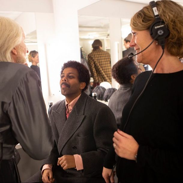 Bilde av to skuespillere i kostyme som smiler. I forgrunnen en kvinne med hodetelefoner med mikrofon.