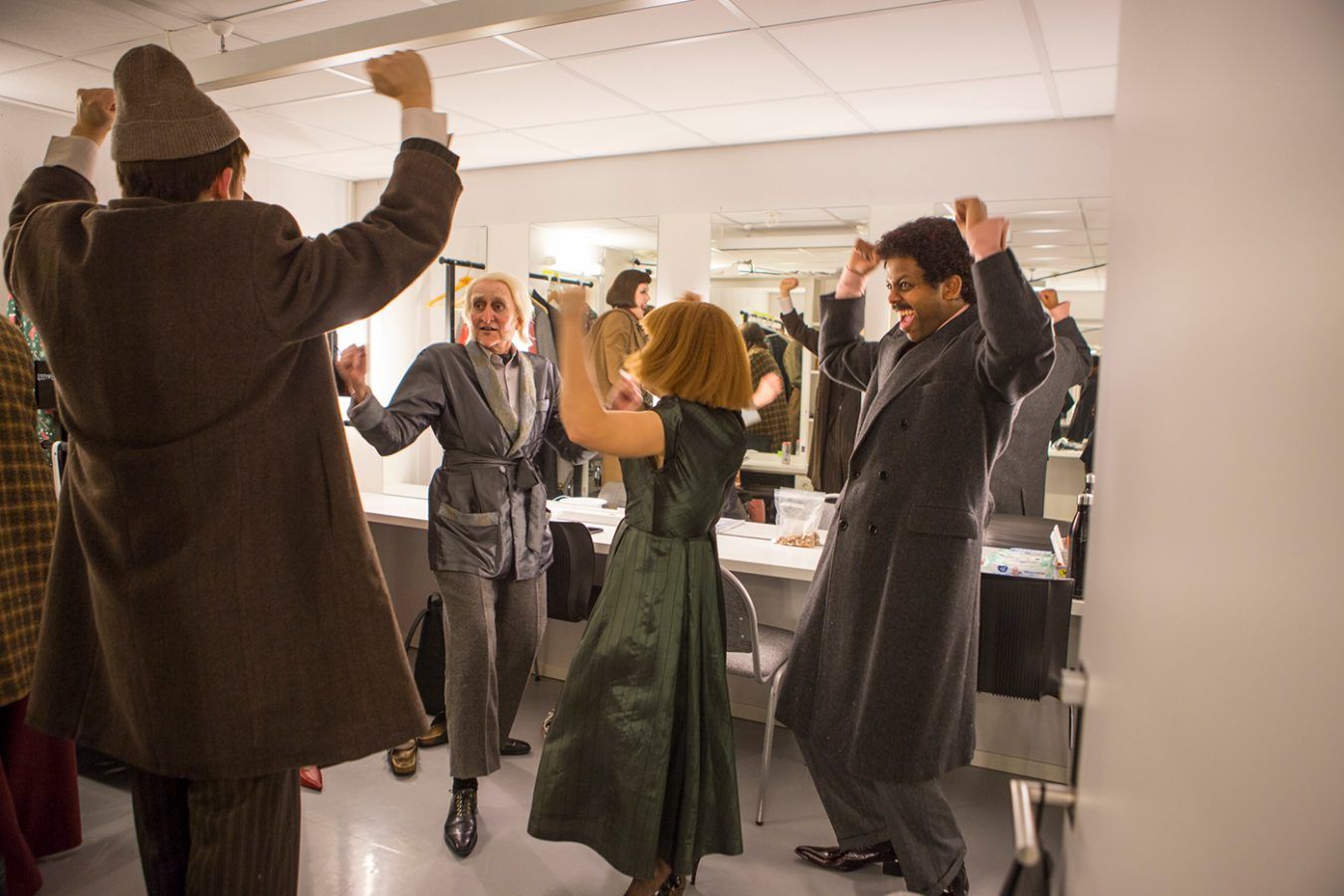 Bilde av jublende skuespillere i kostyme inne i en garderobe.