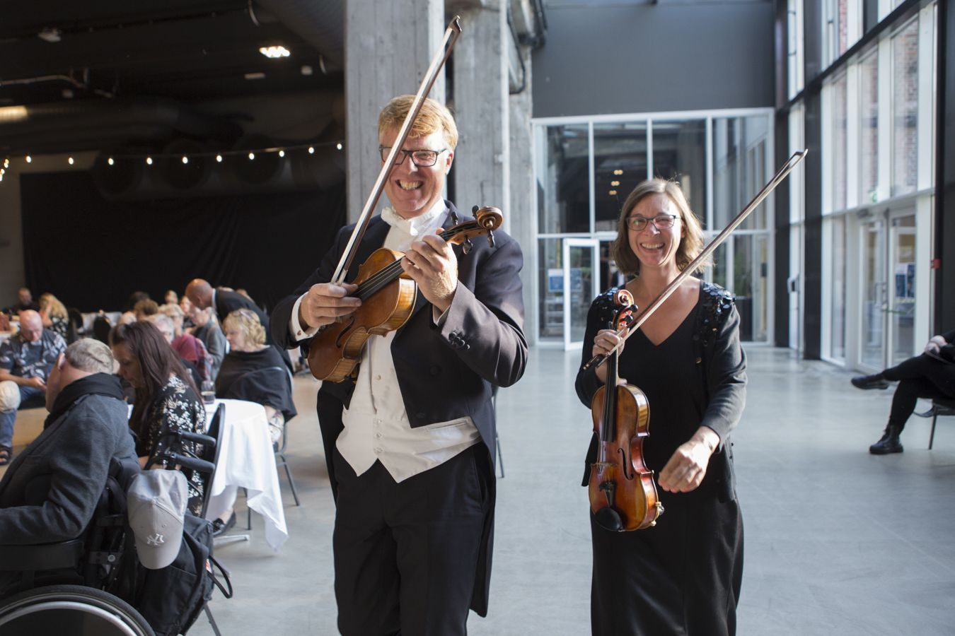 Mannlig og kvinnelig musiker som kommer gående, smilende og bærende på sine fioliner.