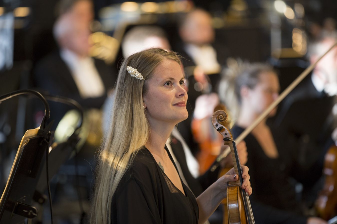 Kvinne med langt lyst hår som sitter i et orkester. Hun holder en fiolin.