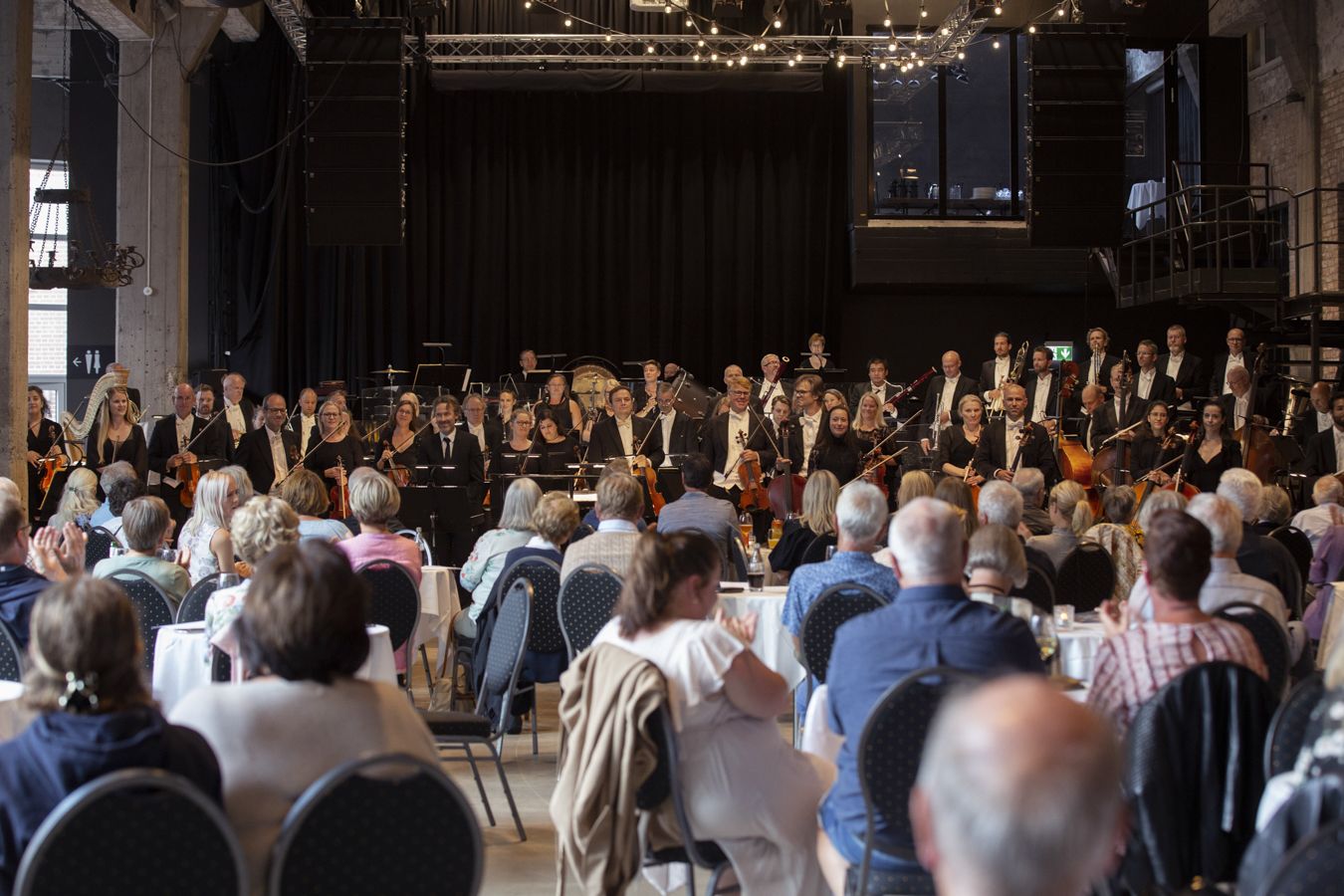 Publikum sett bakenfra og et symfoniorkester som står oppreist.