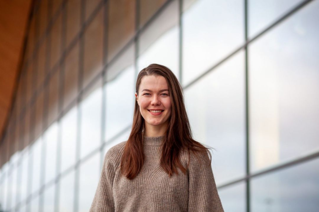 Synne Reichelt Føreland, kostymedesigner. Smilende kvinne med mørkt, langt hår foran glassfasade