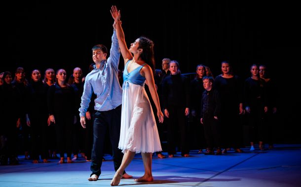 En ung mann og ung kvinne som danser sammen. I bakgrunnen skimtes et kor kledd i sort.