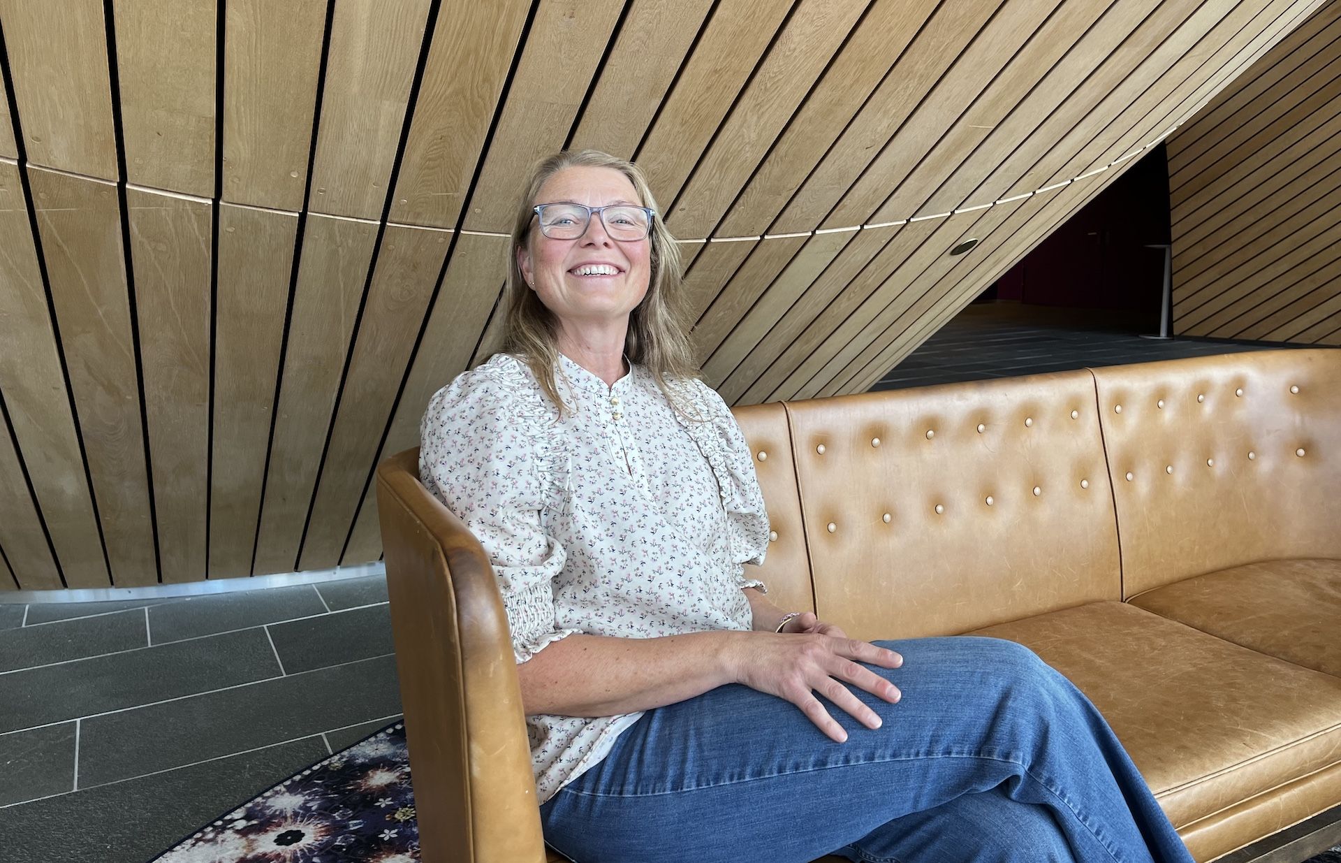 smilende dame som sitter i en sofa i foajeen til kilden teater og konserthus