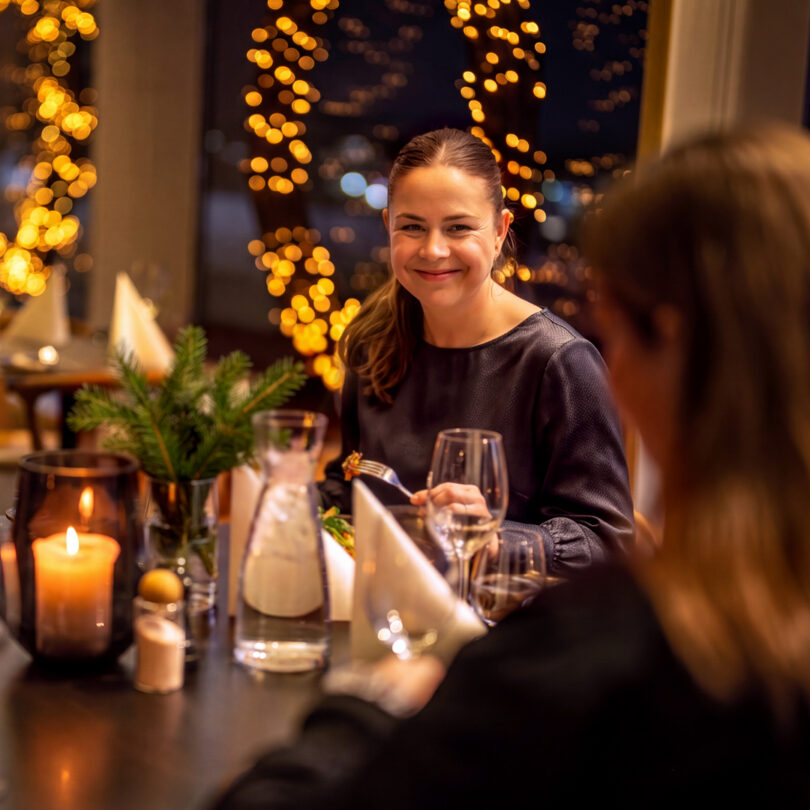 Bilde av kvinne som spiser i Restaurant Frihavn. Det er julebord og varm stemning. Kvinnen smiler til andre ved bordet.
