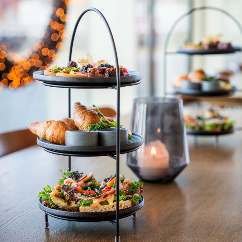 Photo of a three-tiered tray (afternoon tea) with open-faced sandwiches, croissants, and macarons.