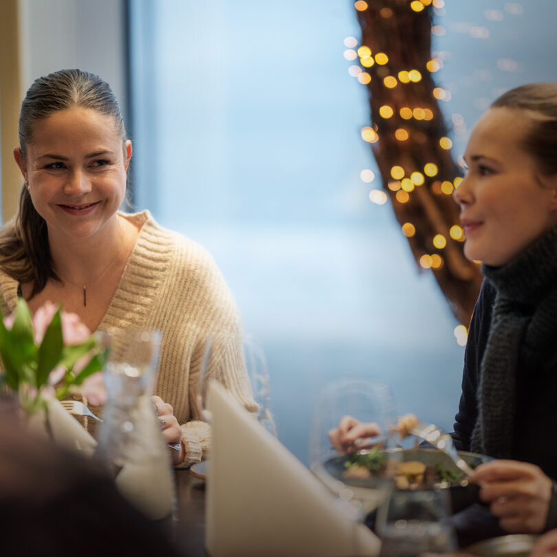 A photo of two women sitting and eating at Restaurant Frihavn. The atmosphere is subdued, with Christmas lights in the background.