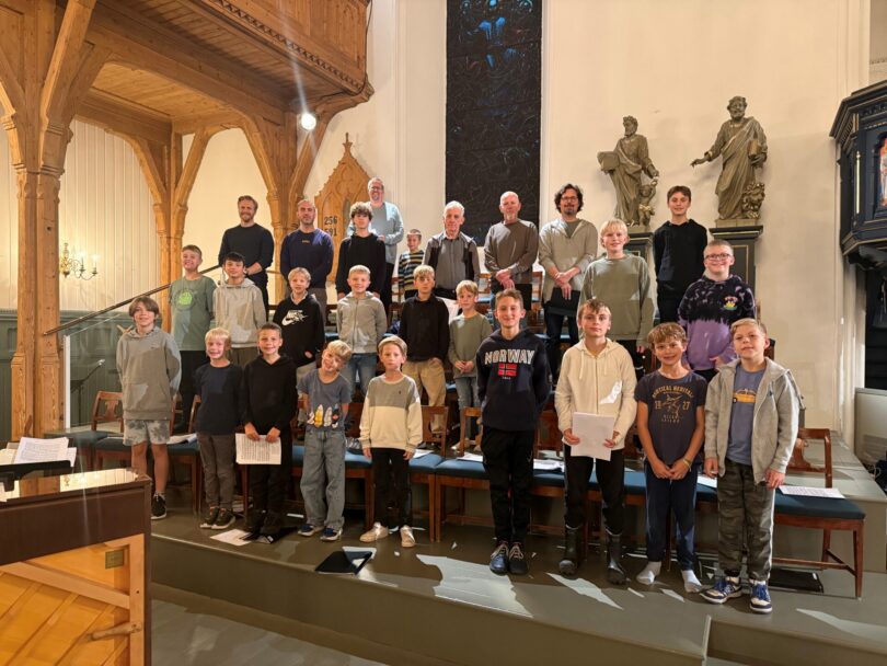 Gruppebilde av et barnekor sammen med flere voksne, oppstilt i flere rekker inne i en kirke.